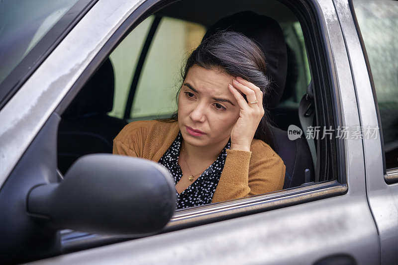 悲伤的西班牙裔年轻女子坐在车里的驾驶座上感到焦虑和压力