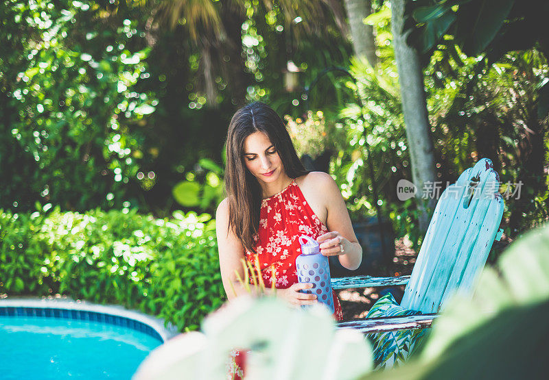 一名女子在热带地区的户外泳池边放松，泳池里有可重复使用的水瓶