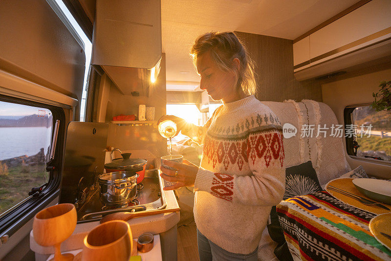 日落时分，女人在她的露营车里做饭，面包车生活概念。