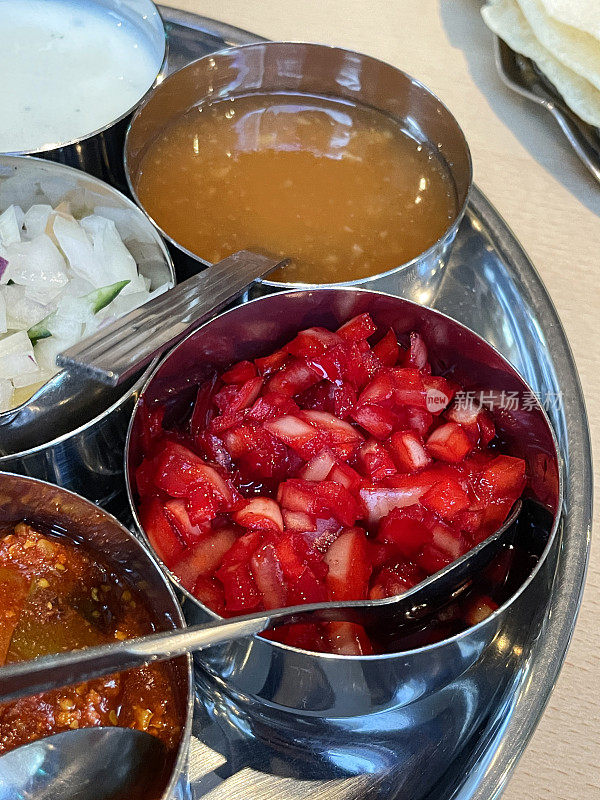 印度调味品金属碗，茶匙，蘸料包括红洋葱酸辣酱，raita(酸奶酱)，切碎的洋葱，芒果酸辣酱和酸橙泡菜的特写图像，重点放在前景，升高的视图