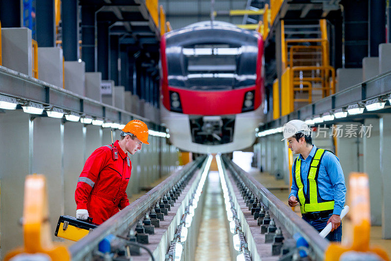 专业的工程师和技术工人在工厂车间讨论并留在列车前检查电气或空轨列车的轨道功能。