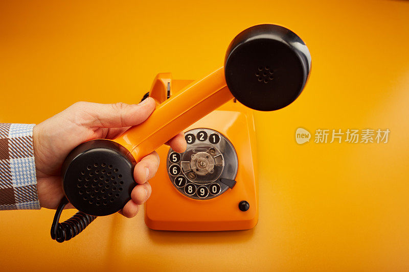 接到一个电话。拿着一个老式的电话听筒。拿着一个橙色的复古电话听筒，背景是橙色