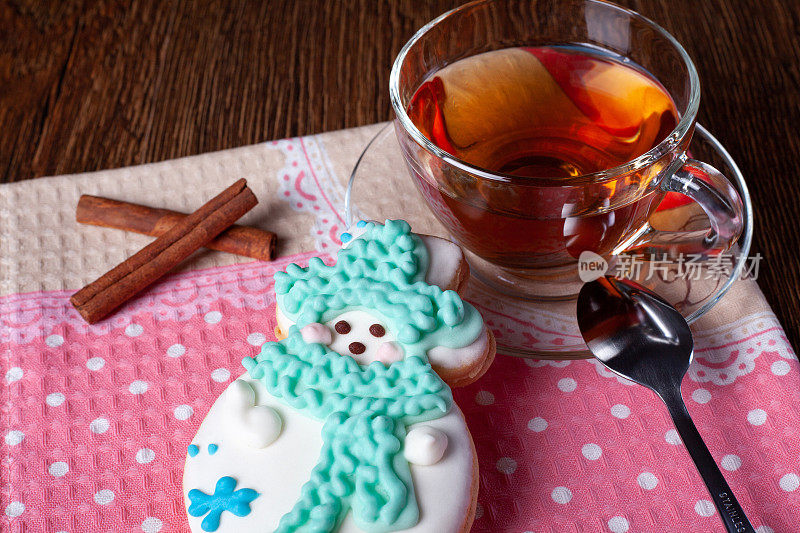 像雪人一样装饰的姜饼和粉红色餐巾上盛着茶的玻璃杯。节日姜饼和茶