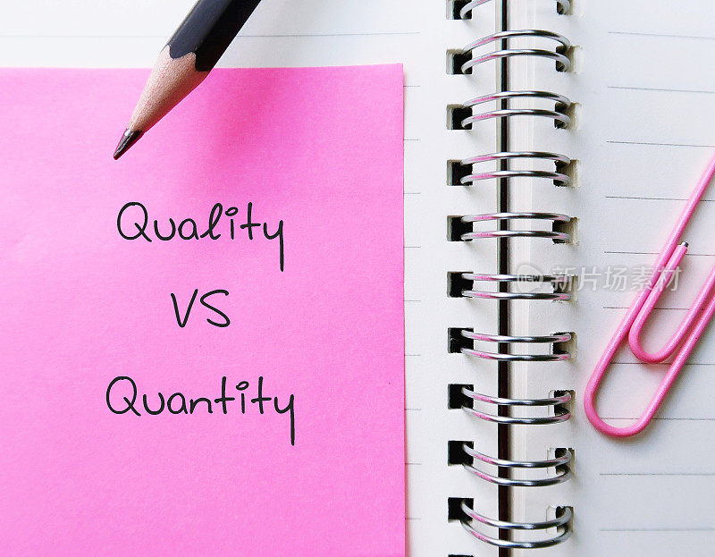粉色笔记夹在笔记本上，手写文字“质量VS数量”，比较衡量某物的好坏与多少，以确定哪种生产方式最有效