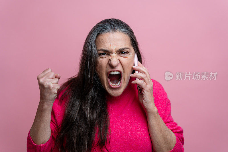 愤怒的高级女性一边打电话一边尖叫。粉红色背景隔离