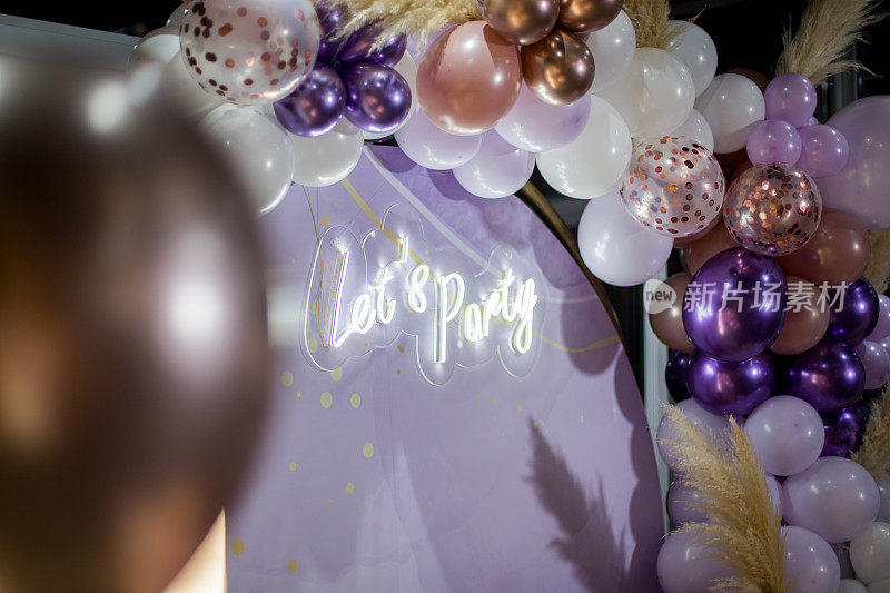 派对装饰用紫色-白色气球和潘帕斯草原，灯光文字“让我们聚会”。