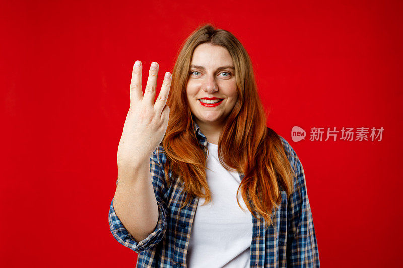 伸出三个手指的手。30多岁的年轻女子在孤立的红色背景下快乐地用手指数三，摄影棚拍摄。