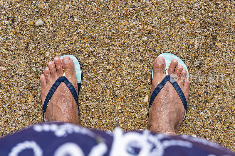 沙滩上男人穿着人字拖的脚。前视图。平的。本空间
