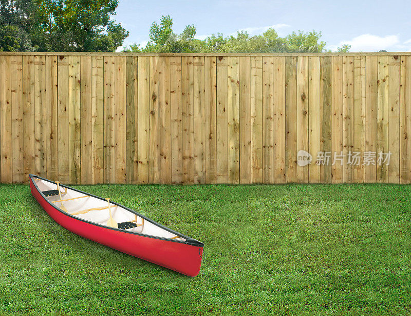 一艘红色的皮艇停在空旷的后院，周围是绿草和木栅栏