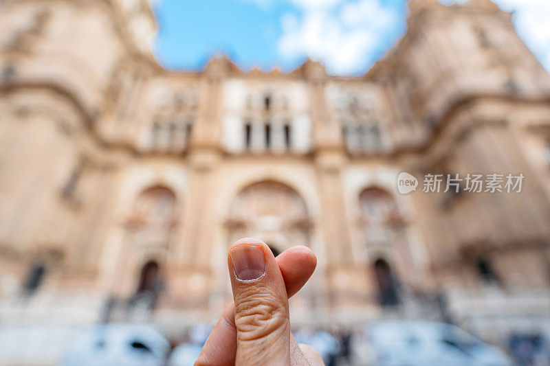 在西班牙Málaga的一座大教堂前，一个年轻人在做一个手指心形