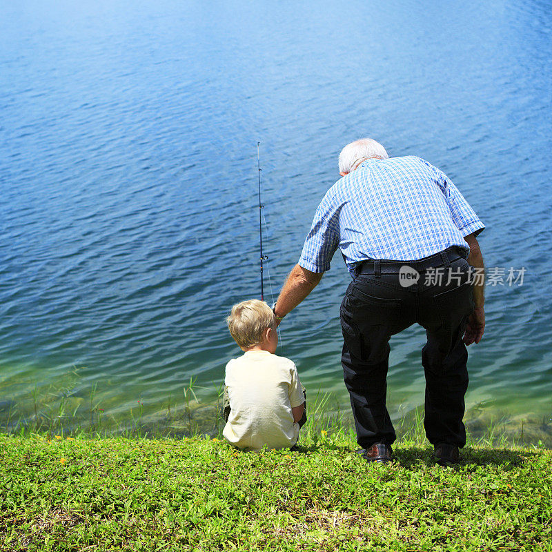 后视图的一个男孩钓鱼与他的爷爷在一个蓝色的湖