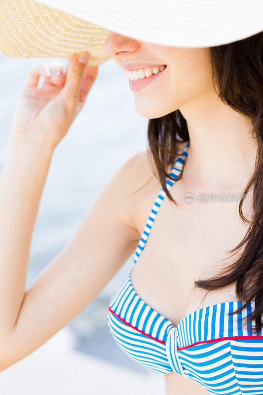 年轻女子在比基尼和太阳帽微笑在海边