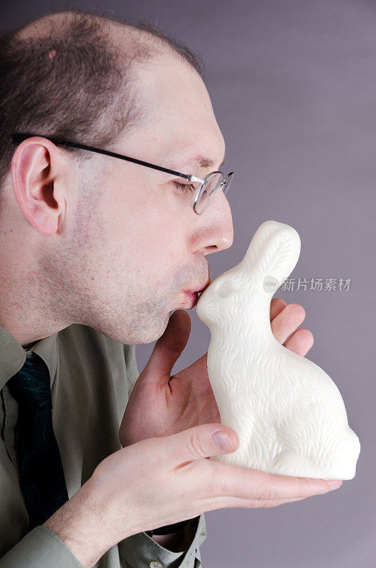 中年男人亲吻白巧克力兔子。
