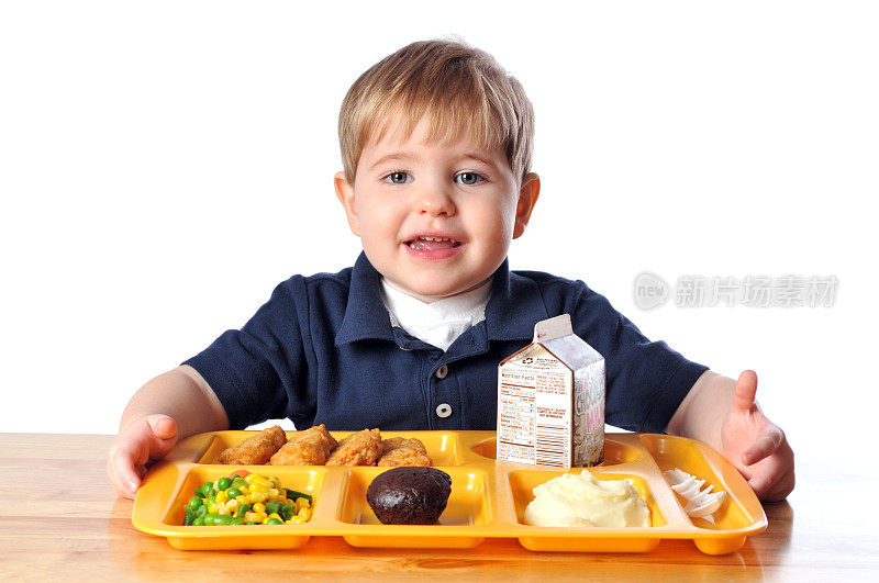 小男孩坐在桌子旁和他的学校午餐