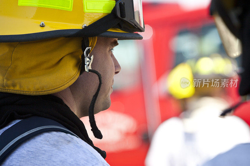 肖像消防队员看着行动与消防车在背景