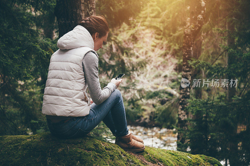 年轻女性旅行者在森林里使用智能手机
