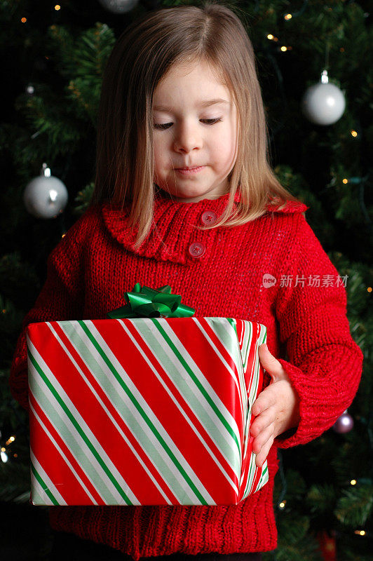 小女孩在圣诞树旁拿着圣诞礼物
