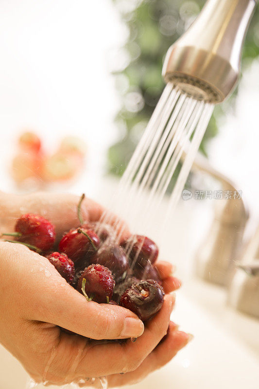 食物:在厨房水槽里洗新鲜熟樱桃的女人。