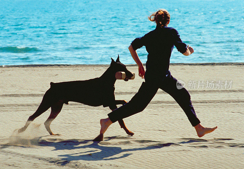 一个女人和她的杜宾犬在沙滩上奔跑玩耍