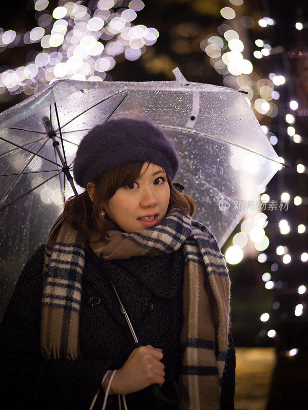 年轻女子站在雨中，挂着圣诞彩灯