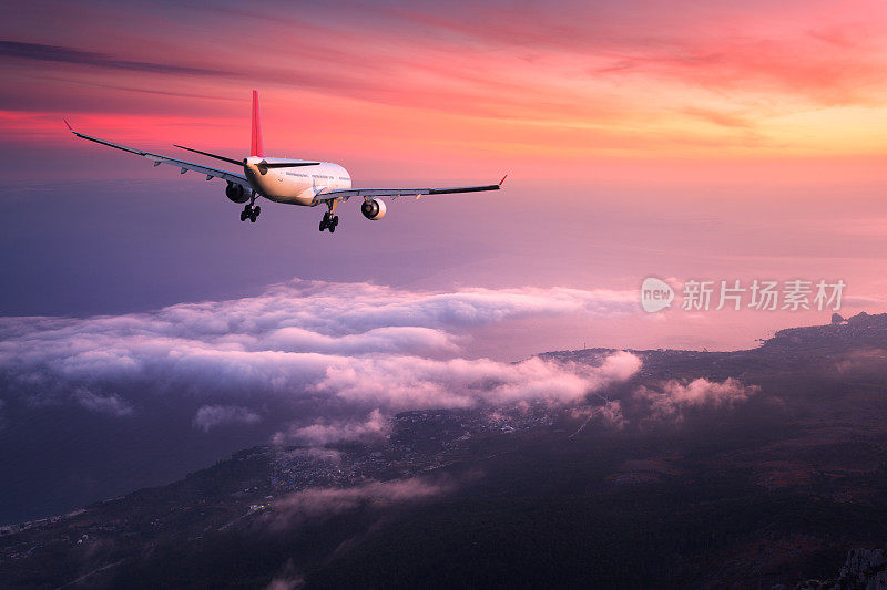 飞机。风景与巨大的白色客机是飞行在红色的天空之上的云彩在彩色日落。的旅程。客机在黄昏时分降落。商务旅行。商用飞机