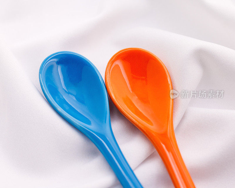 白色织物背景上的蓝色和橙色陶瓷勺。色彩斑斓的概念。