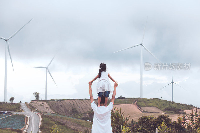 亚洲小女孩的背影站在父亲的肩膀上，一起在风力涡轮机场玩耍
