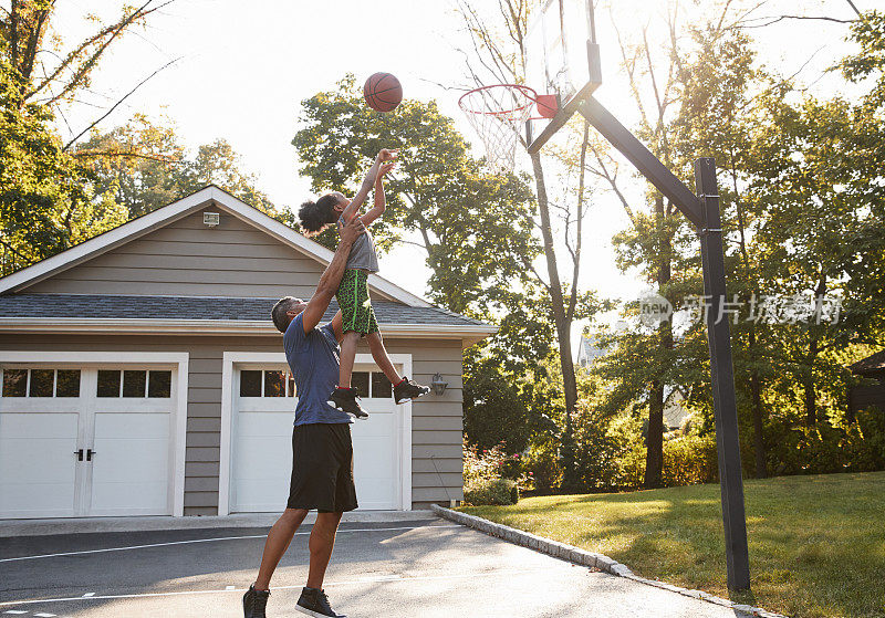爸爸和儿子在家里的车道上打篮球