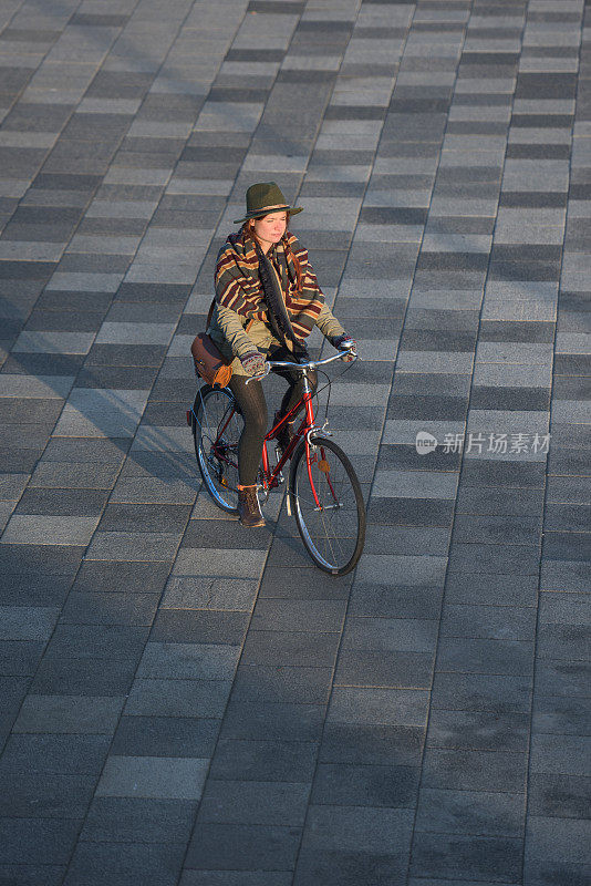 在城市广场上骑着老式自行车的姜黄色女人