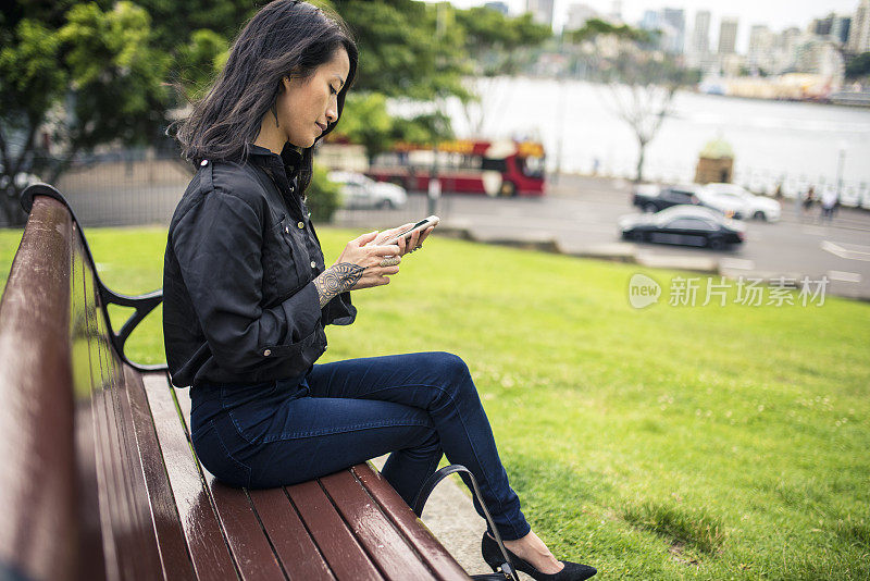 坐在长椅上玩智能手机的亚洲女性