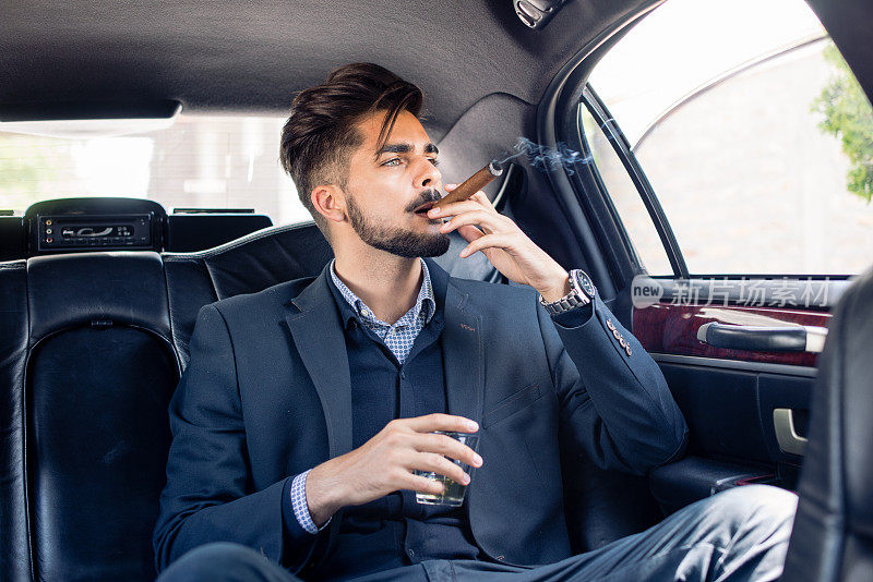 年轻的商人在豪华轿车里享受雪茄和美酒