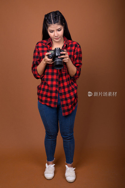 工作室拍摄的年轻美丽的亚洲女子穿着红色格子衬衫与相机的彩色背景