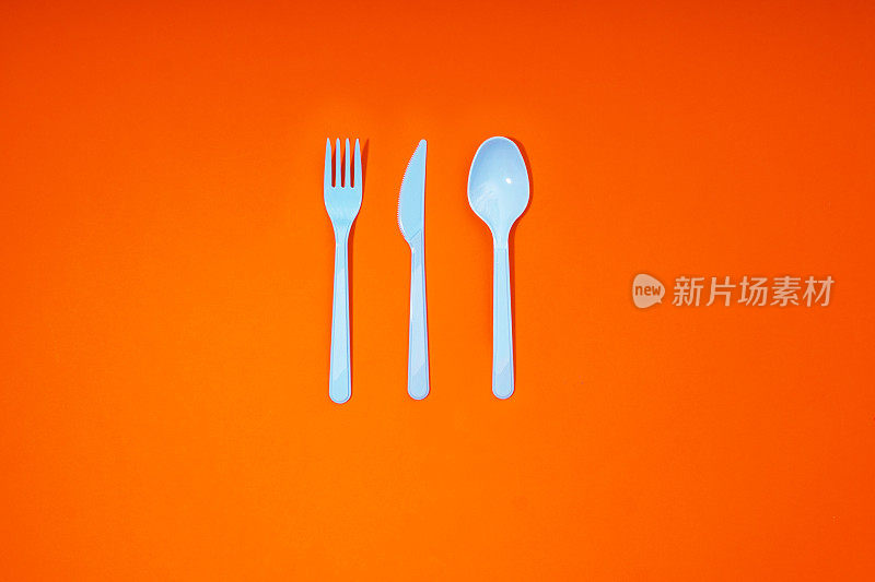 橙色背景的塑料餐具，勺子，刀和叉