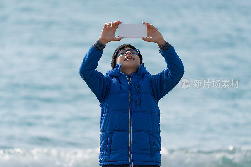 快乐男孩在海滩上散步，用手机自拍