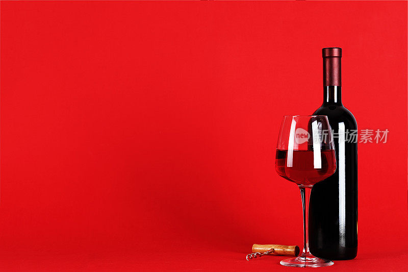 红酒置于红色背景上-一瓶红酒与一只盛满酒的酒杯置于红色背景上