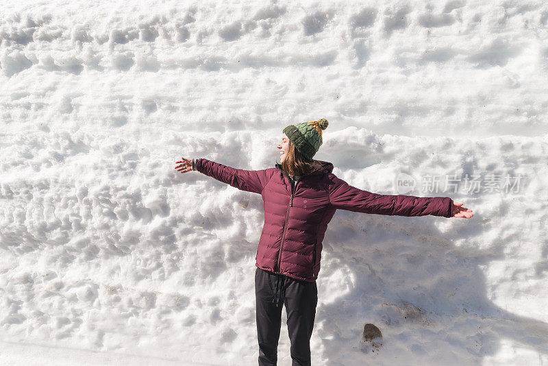 一位女性徒步旅行者站在雪堆前，开怀大笑