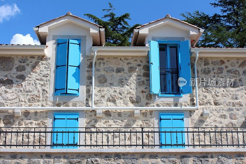 新建成的地中海式别墅窗户上开闭的浅蓝色木质百叶窗，传统的石材风格，带前阳台