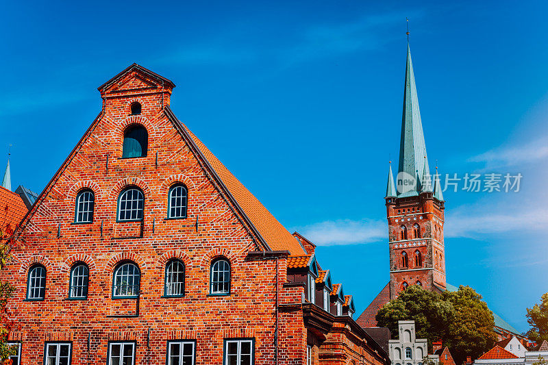 红砖历史盐库建筑。在蓝色天空的背景下，有翡翠绿的尖顶的教堂塔。吕贝克，石勒苏益格-荷尔斯泰因，德国北部