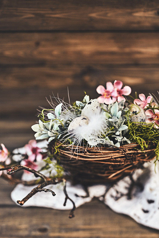 鹌鹑蛋与花和羽毛巢在质朴的木头桌子上