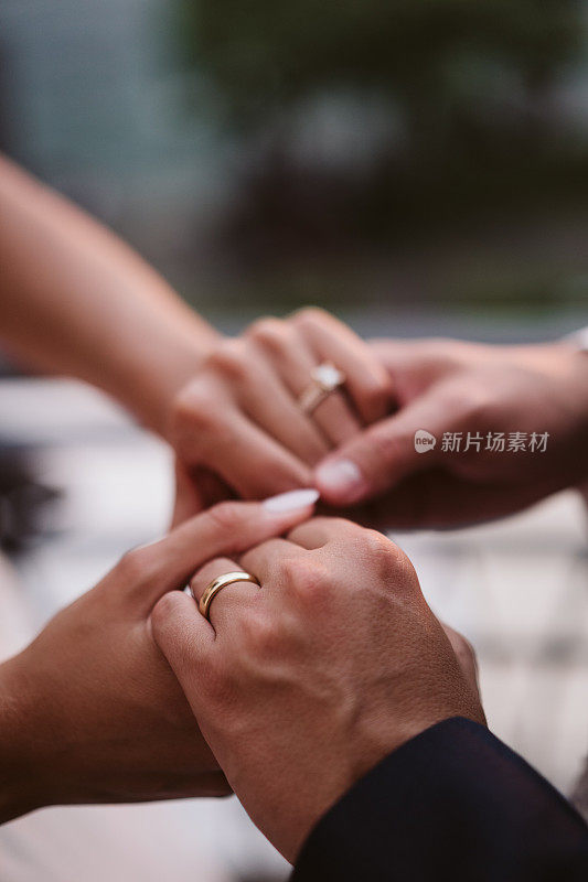 在一个阳光明媚的日子里，新娘和新郎牵手的特写镜头。结婚戒指的细节。