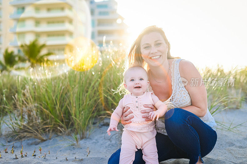 美丽的年轻母亲抱着襁褓中的女儿在田园诗般的海滩上