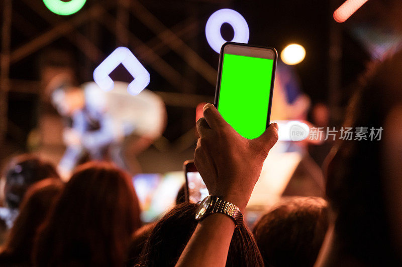 在晚会上，观众们用绿色屏幕的手机拍照。
