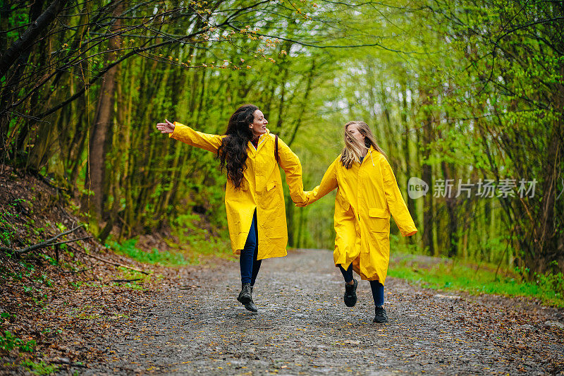 两个穿着雨衣的女性朋友在雾霾的森林里在雨中奔跑