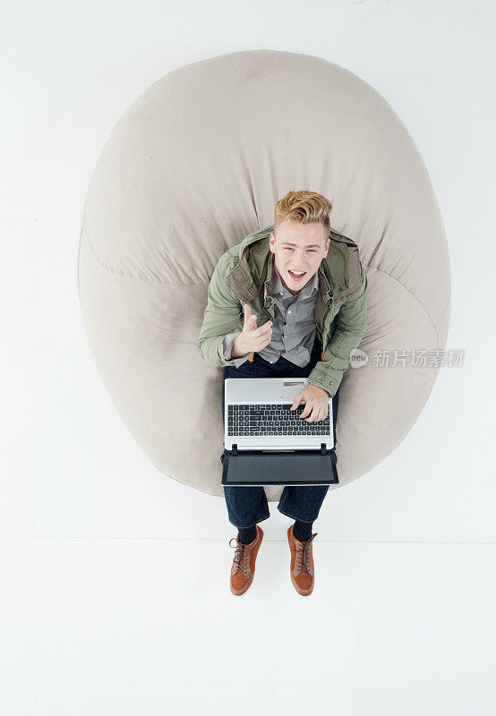 白种人男孩在白色背景前休息，穿着暖和的衣服，使用笔记本电脑