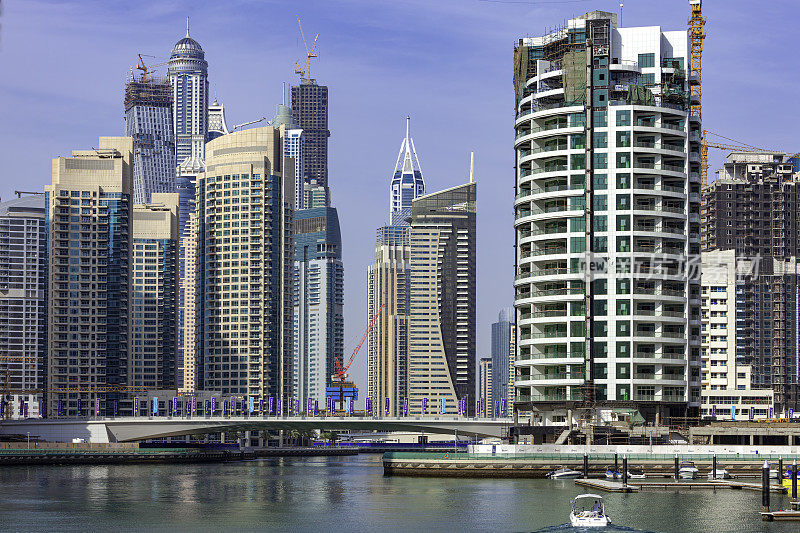 迪拜，阿拉伯联合酋长国-看着对面的水域迪拜码头的高滨水摩天大楼的背景在蓝色的下午天空。一些塔正在建设中。