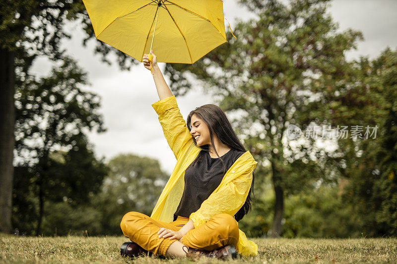 美丽的年轻女子穿着黄色雨衣，拿着黄色雨伞在户外