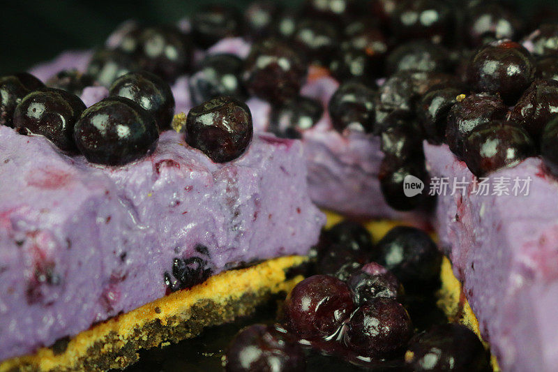 这是切片蓝莓芝士蛋糕的特写，以黄油饼干为底，以黑色为背景，蓝莓马斯卡彭奶油芝士甜点布丁，上面点缀着新鲜的蓝莓