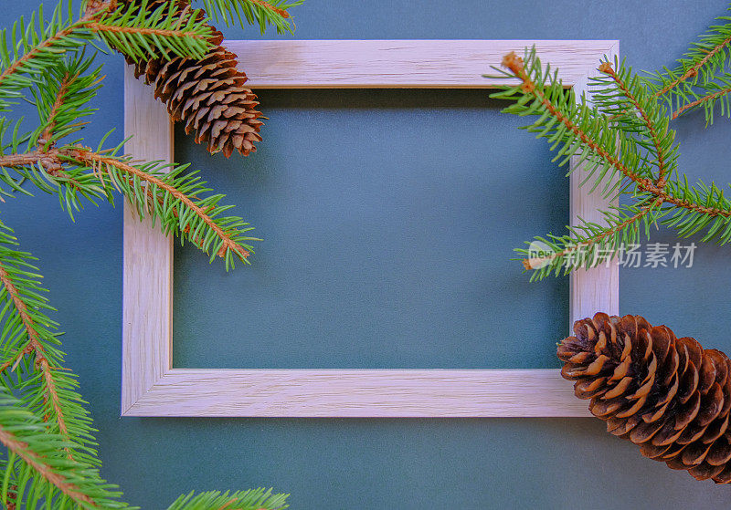 木画框横跨冷杉树枝和球果。圣诞模型与冷杉树枝，球果在蓝色的背景。前视图。平的。副本的空间。圣诞明信片