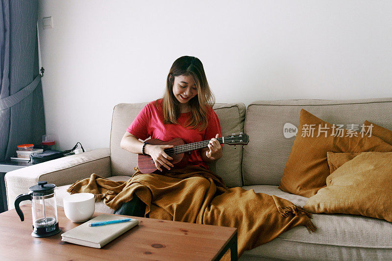 美丽的中国女人在家里弹奏尤克里里