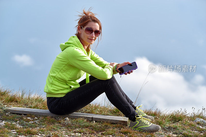 美丽的女人坐在山边拿着智能手机